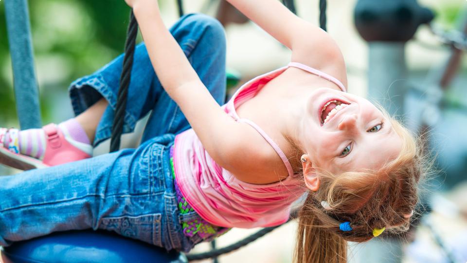 En glad liten flicka som klättrar i en klätterställning på en lekplats.