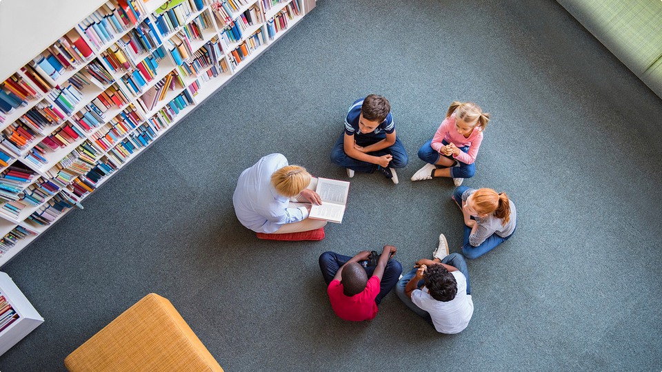 Barn sitter på golvet i ring och lyssnar på en person som läser sagor på biblioteket.
