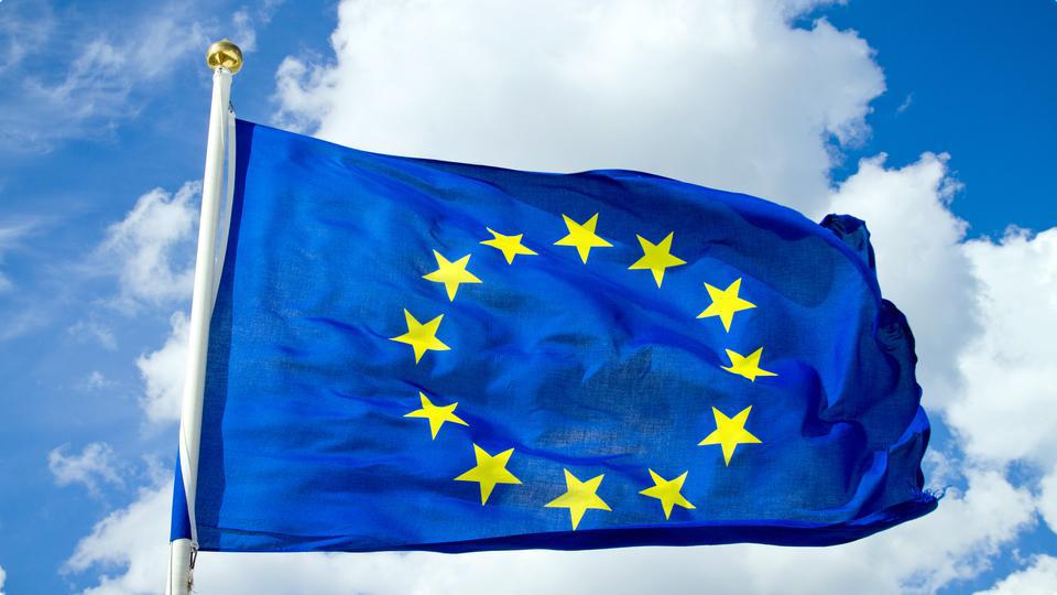 EU-flaggan vajar i vinden en fin sommardag med vita lätta moln i bakgrunden.