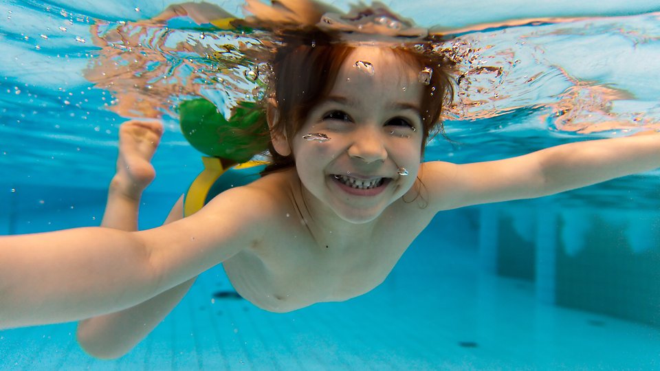 Barn som simmar under vatten i bassäng