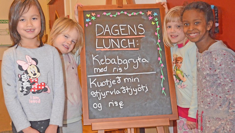 Fyra barn som står vid en matsedel för skolmat. Text både på svenska och älvdalska.